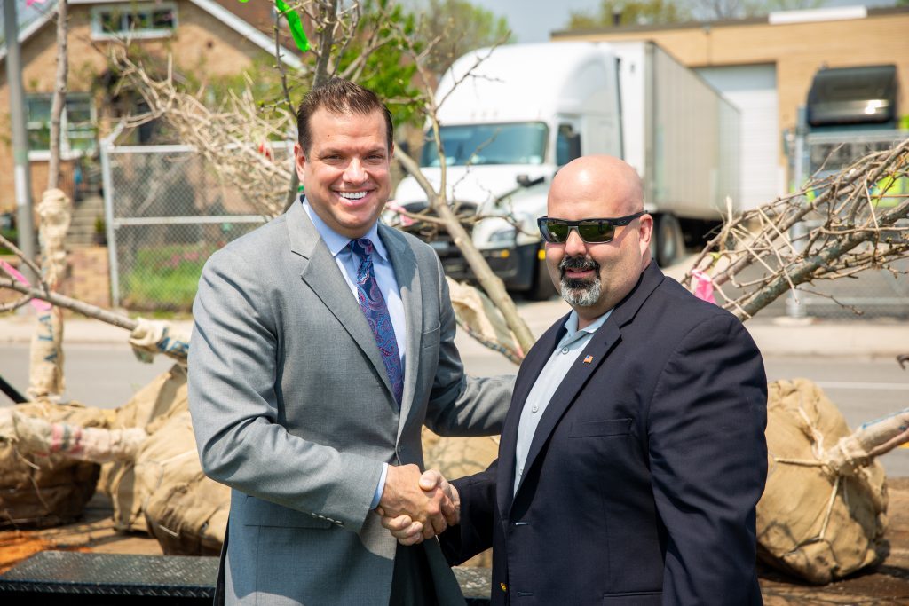 Lyons Mayor Chris Getty (left) and McCook Mayor Terry Carr shake hands in front of some of the 172 trees being planted along 47th Street between their communities. (Supplied photo)