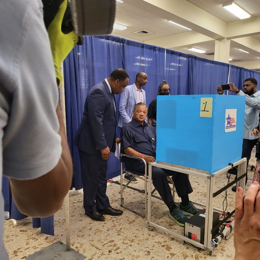 Democrat Jonathan Jackson (standing, at left) helps his famous father, the Rev. Jesse L. Jackson Sr. (seated), vote on June 28. --Supplied photo