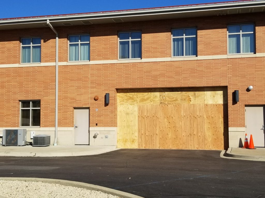 The rear garage door of the Hodgkins Village Hall is boarded up after a car crashed into the door last week. (Photo by Carol McGowan)