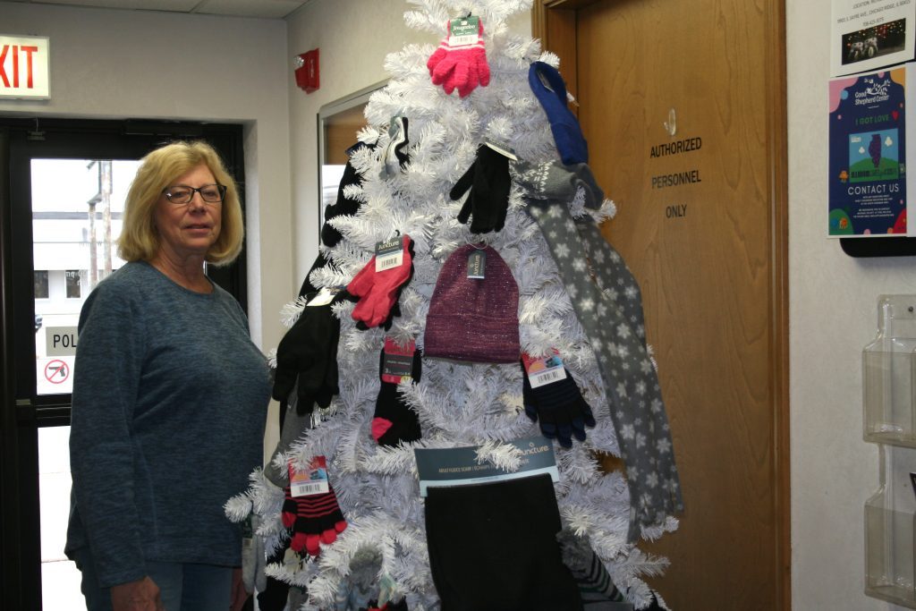 Worth Village Clerk Bonnie Price stands alongside the Mitten Tree, which can be found in the Worth Village Hall. Residents can drop off gloves, mittens, hats or scarves for those in need this holiday season up until Dec. 12. (Photo by Joe Boyle)