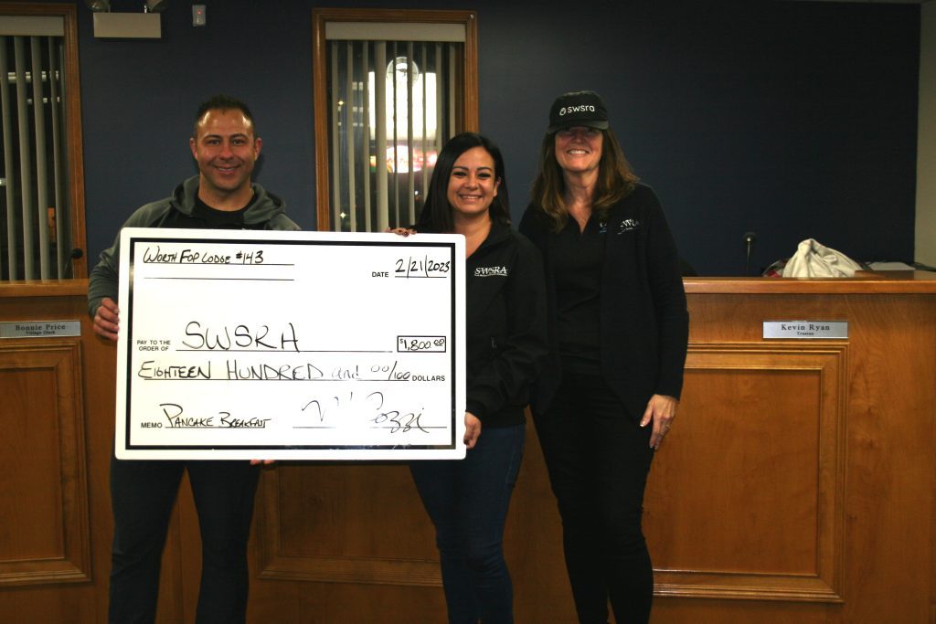The Worth Fraternal Order of Police presented a $1,800 check to the South West Special Recreation Association from the proceeds raised at a recent pancake breakfast. Worth Police Sgt. Mike Cozzi presents the check to (center) Nicolette Lahman, executive director of SWSRA, and Dawn Kehoe, the organization's business manager, during the Worth Village Board meeting Tuesday night. (Photo by Joe Boyle)