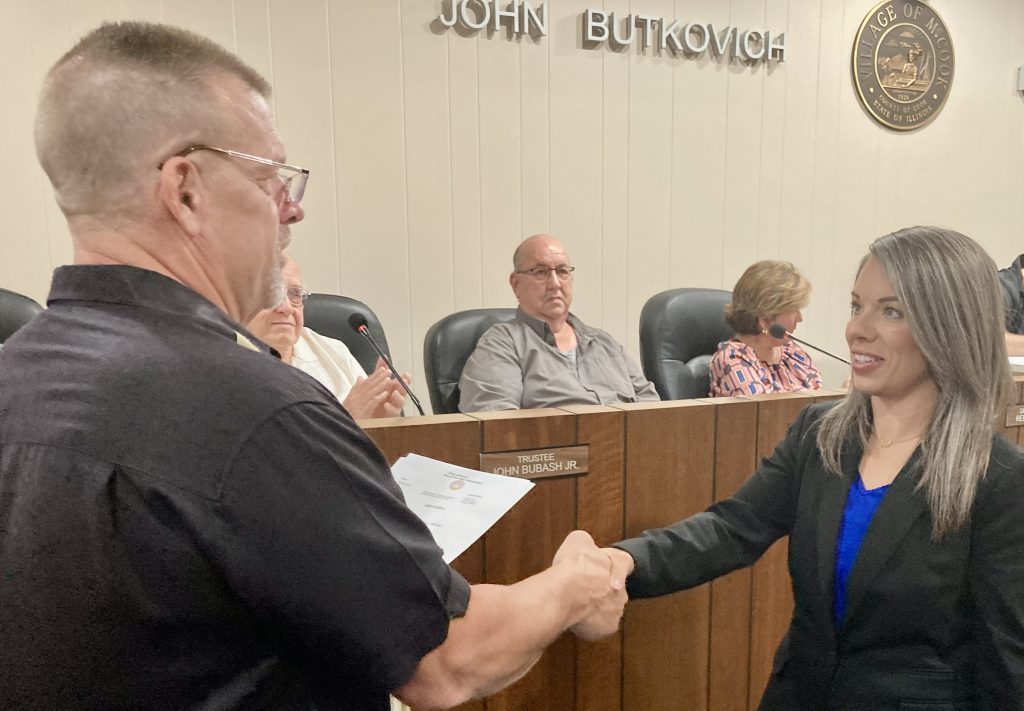 McCook’s newest police officer, Jenna Calderone, shakes hands with Police Commissioner Ken Lyons after she was sworn in at the Aug. 21 village board meeting. Village Trustee Thomas Perrin looks on. (Photo by Steve Metsch) 